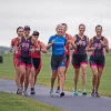 Группа бегуний из клуба бежит с тренером в футболке Trainingpeaks