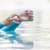 женщина в купальнике с длинными рукавами чешет запястье в бассейне