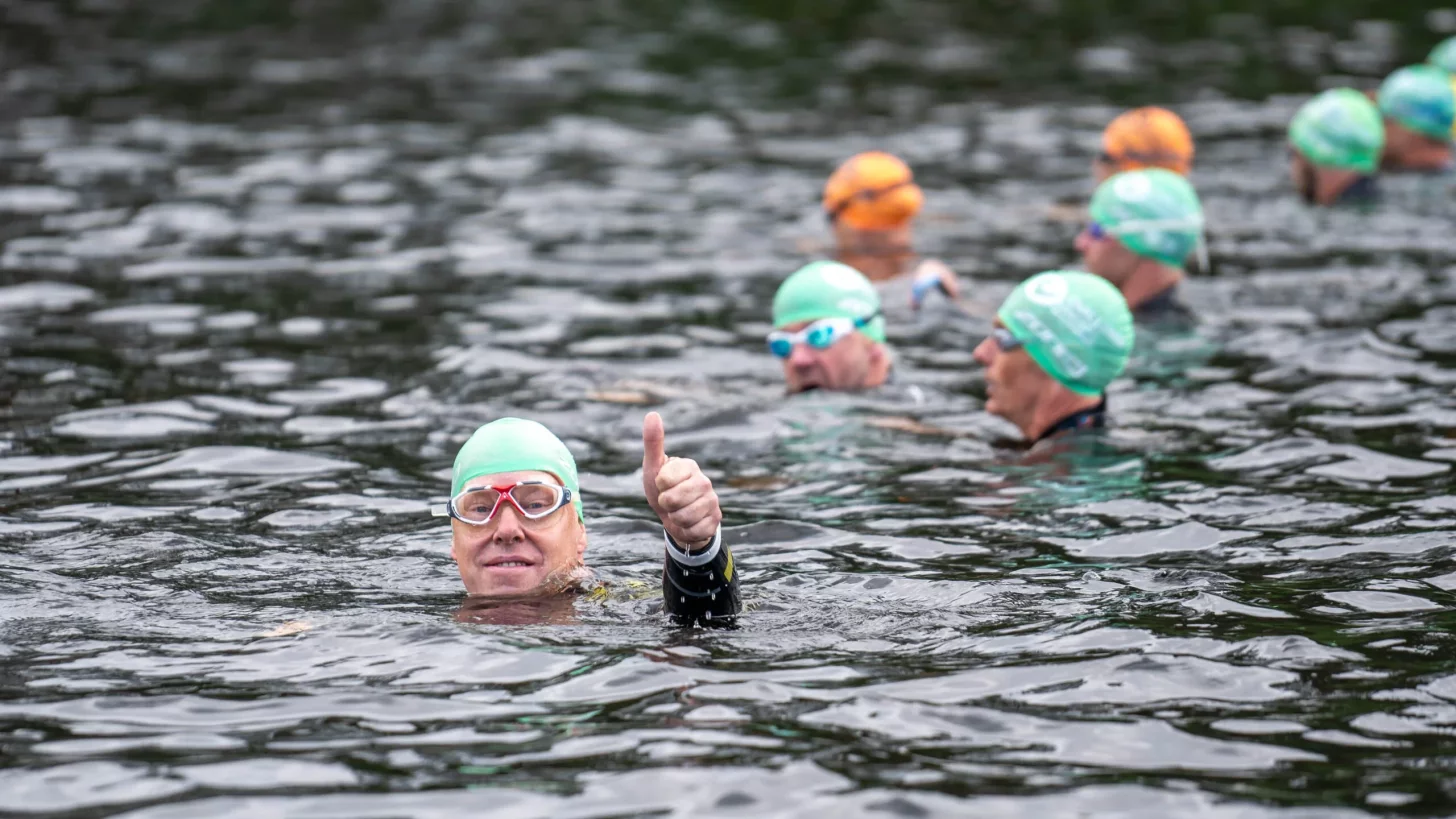мужчина в гидрокостюме и плавательной шапочке, стоящий в воде и показывающий палец вверх на камеру мужчина в гидрокостюме и плавательной шапочке, стоящий в воде и показывающий палец вверх на камеру