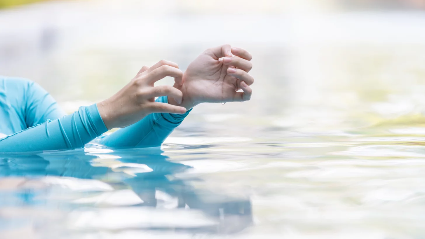 женщина в купальнике с длинными рукавами чешет запястье в бассейне