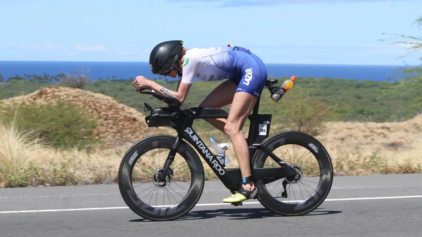 триатлетка возрастной категории чемпионата мира Ironman едет на велосипеде в аэробарах по дороге вдоль океана