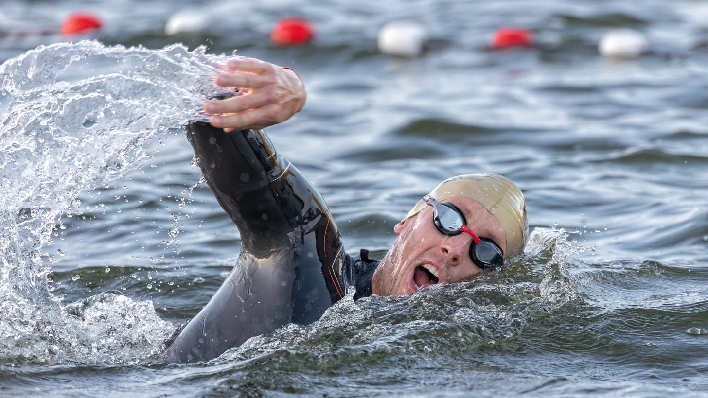 мужчина в плавательной шапочке и гидрокостюме поворачивается, чтобы вдохнуть, плавая в открытой воде