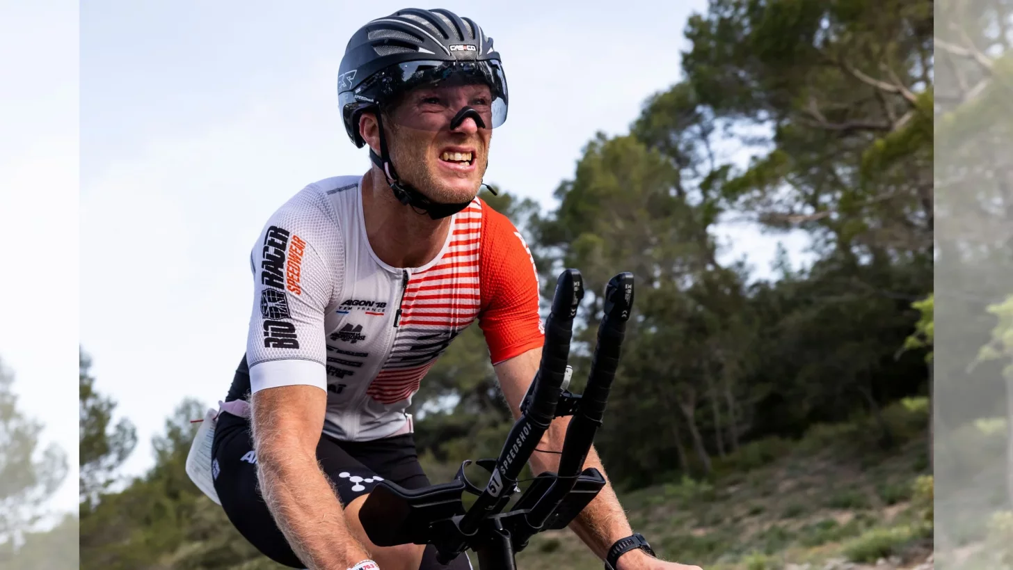 Спортсмен с гримасой на лице едет на своем триатлонном велосипеде против ветра.