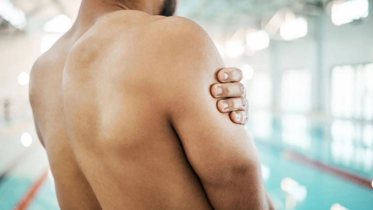 Пловец выполняет упражнения для растяжки и укрепления вращательной манжеты плеча.