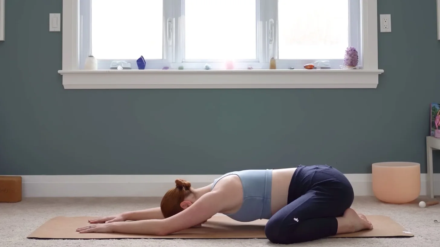 Yoga With Kassandra практикует позу ребенка на коврике, с вытянутыми вперед руками, во время 15-минутного занятия йогой для снятия стресса.
